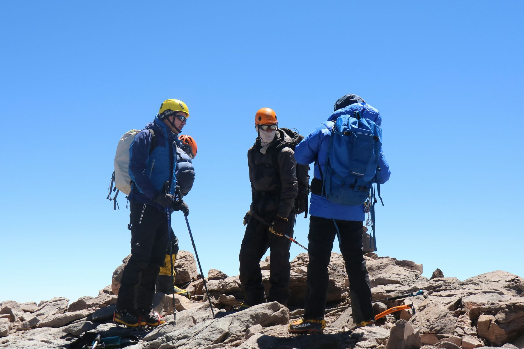 Three trekkers pausing on a rocky ridge under a clear sky